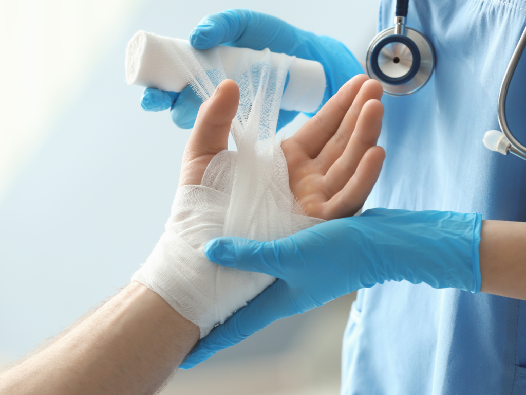 A medical professional with gloves wraps a hand in gauze.