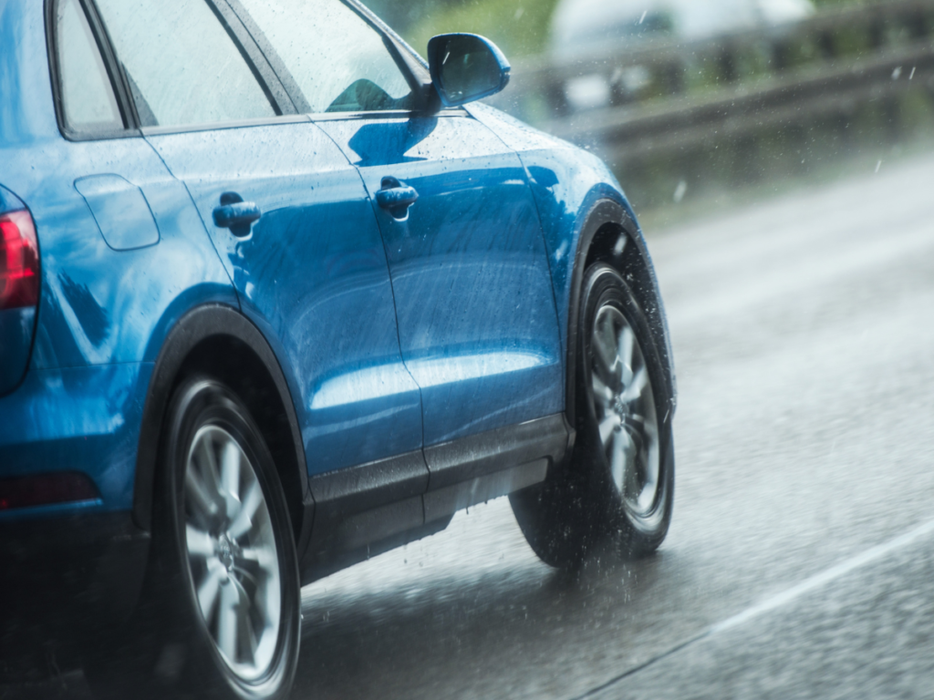 A blue car driving on a road in rain.